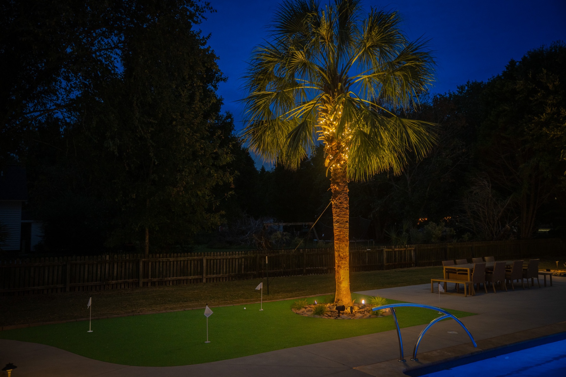 Uplit palm tree over putting green with pool deck at dusk