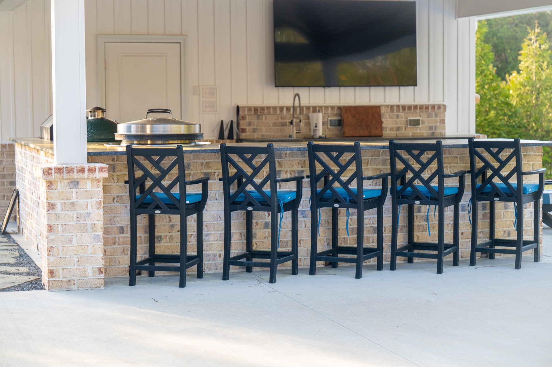 Brick outdoor bar with blue-cushioned stools and mounted TV
