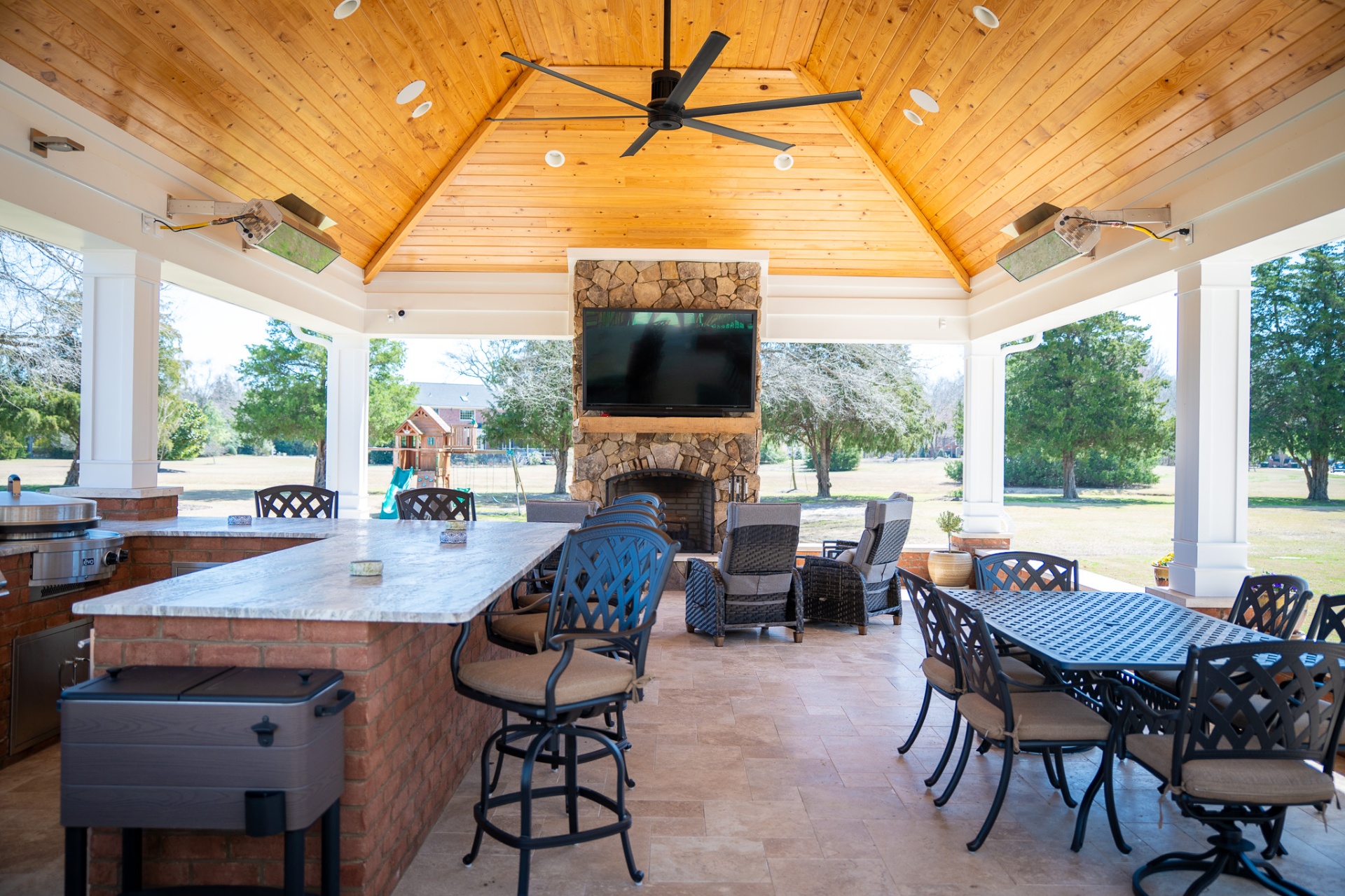 Outdoor pavilion interior with vaulted wood ceiling, fireplace, and bar seating