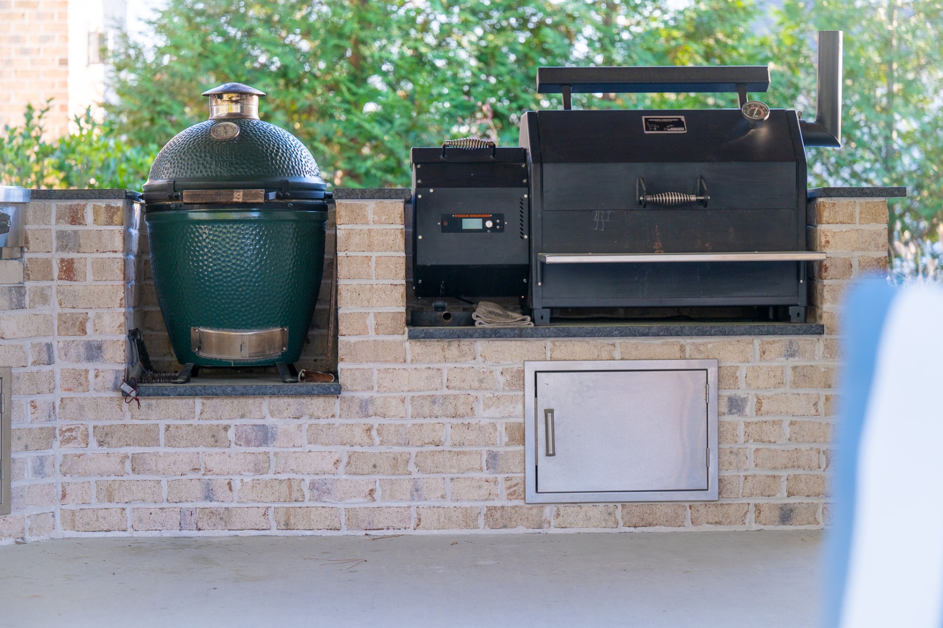 Big Green Egg beside Yoder pellet smoker built into brick counter