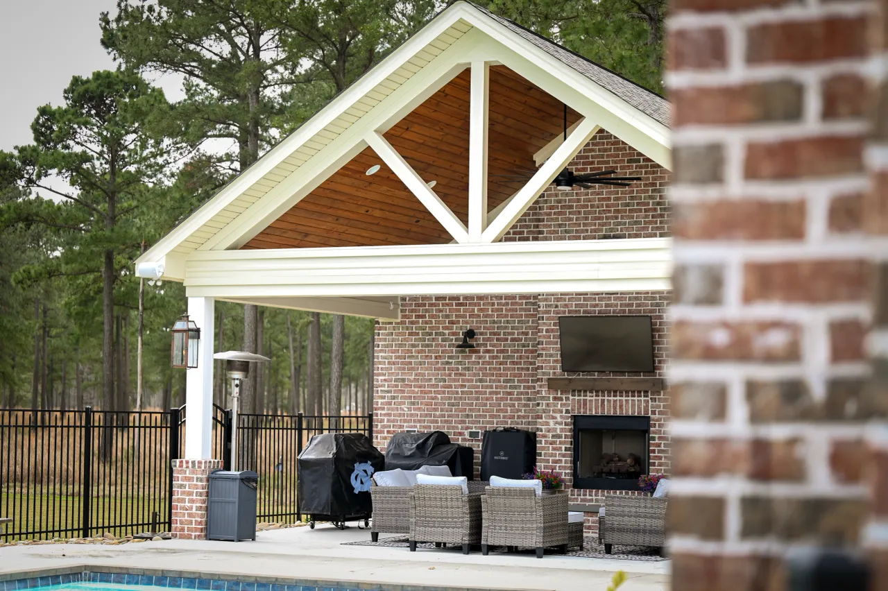 Poolside brick pavilion with vaulted wood ceiling, fireplace, and mounted TV