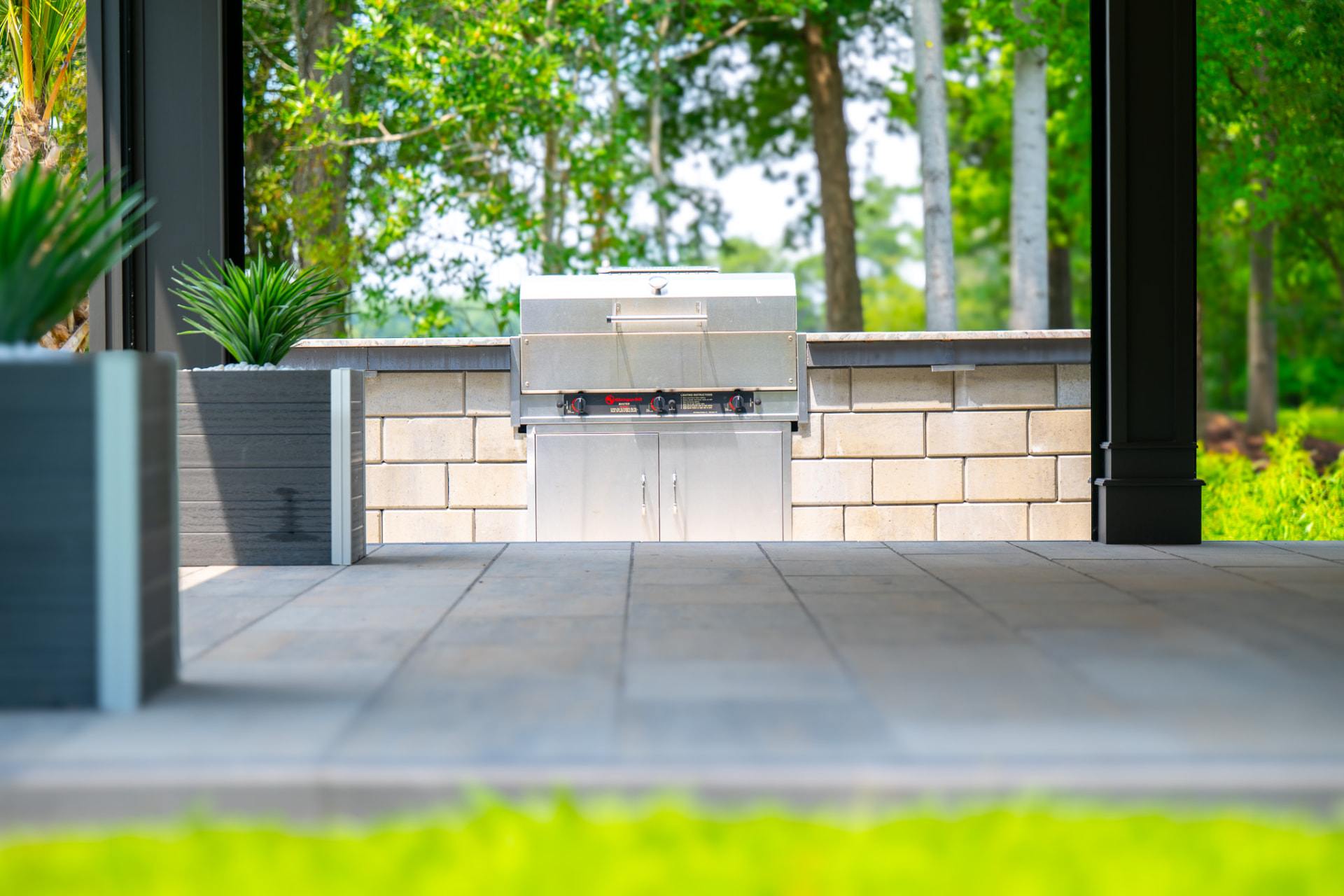Built-in stainless grill set into a stone block wall on a covered paver patio