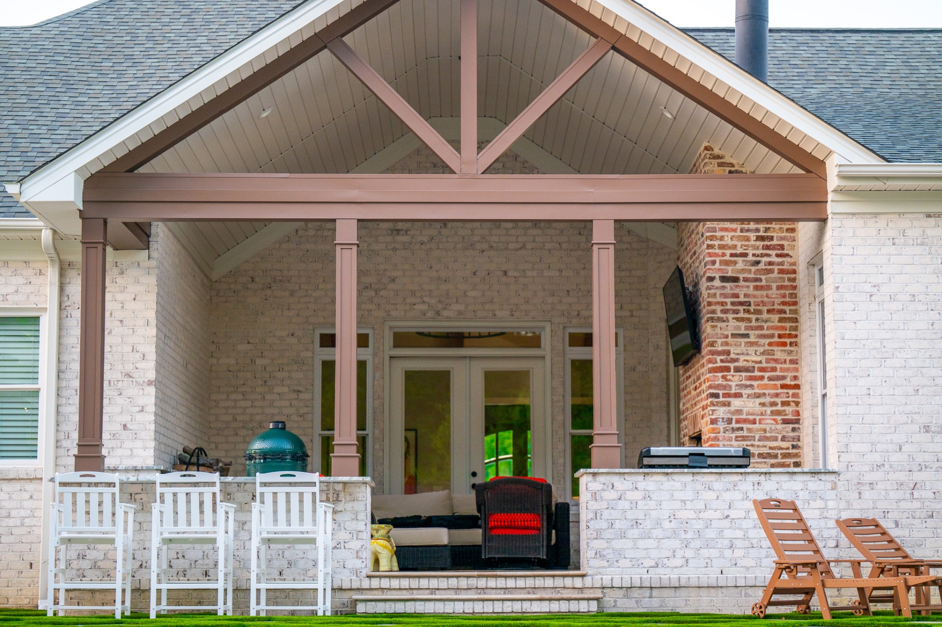 Covered brick porch with a vaulted gable ceiling, outdoor kitchen with Big Green Egg, and lounge seating