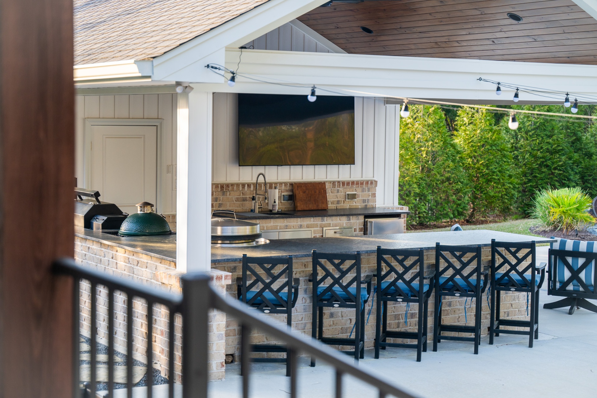 Outdoor bar with mounted TV, Big Green Egg, and Blackstone griddle under pavilion