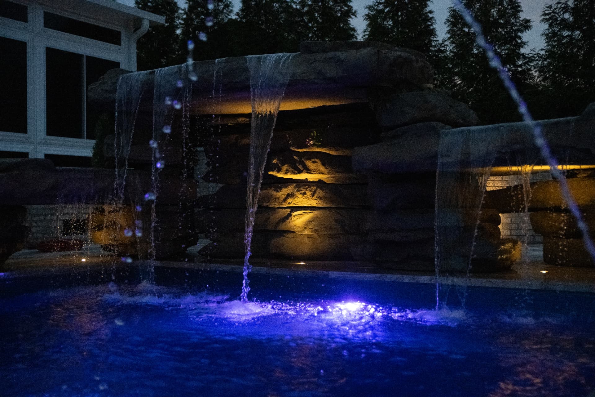 Illuminated rock grotto waterfall spilling into a blue-lit pool at night