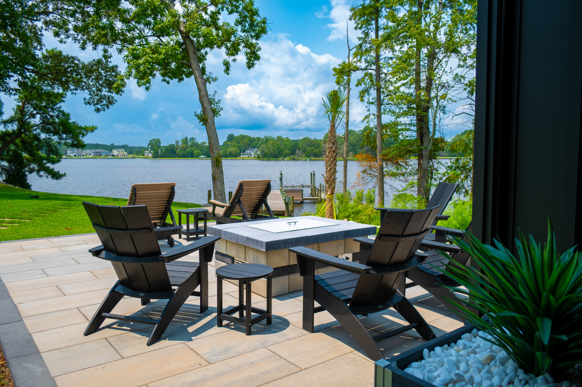 Lakefront paver patio with black Adirondack chairs around a square gas fire table