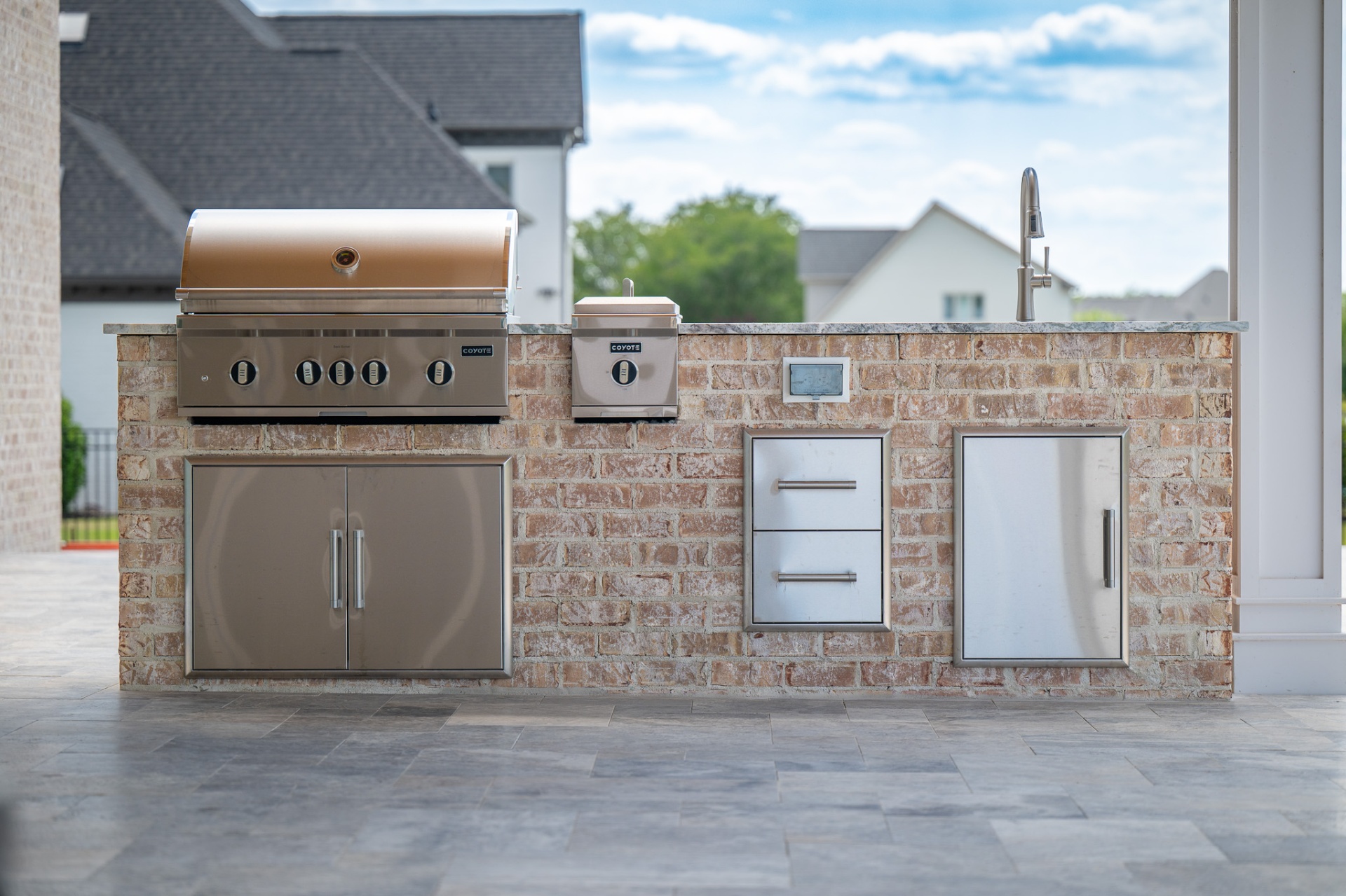 Brick outdoor kitchen with Coyote grill, side burner, and stainless cabinetry