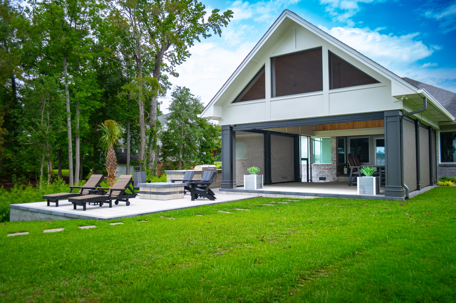 White gable pavilion with motorized screens overlooking a paver patio and manicured lawn