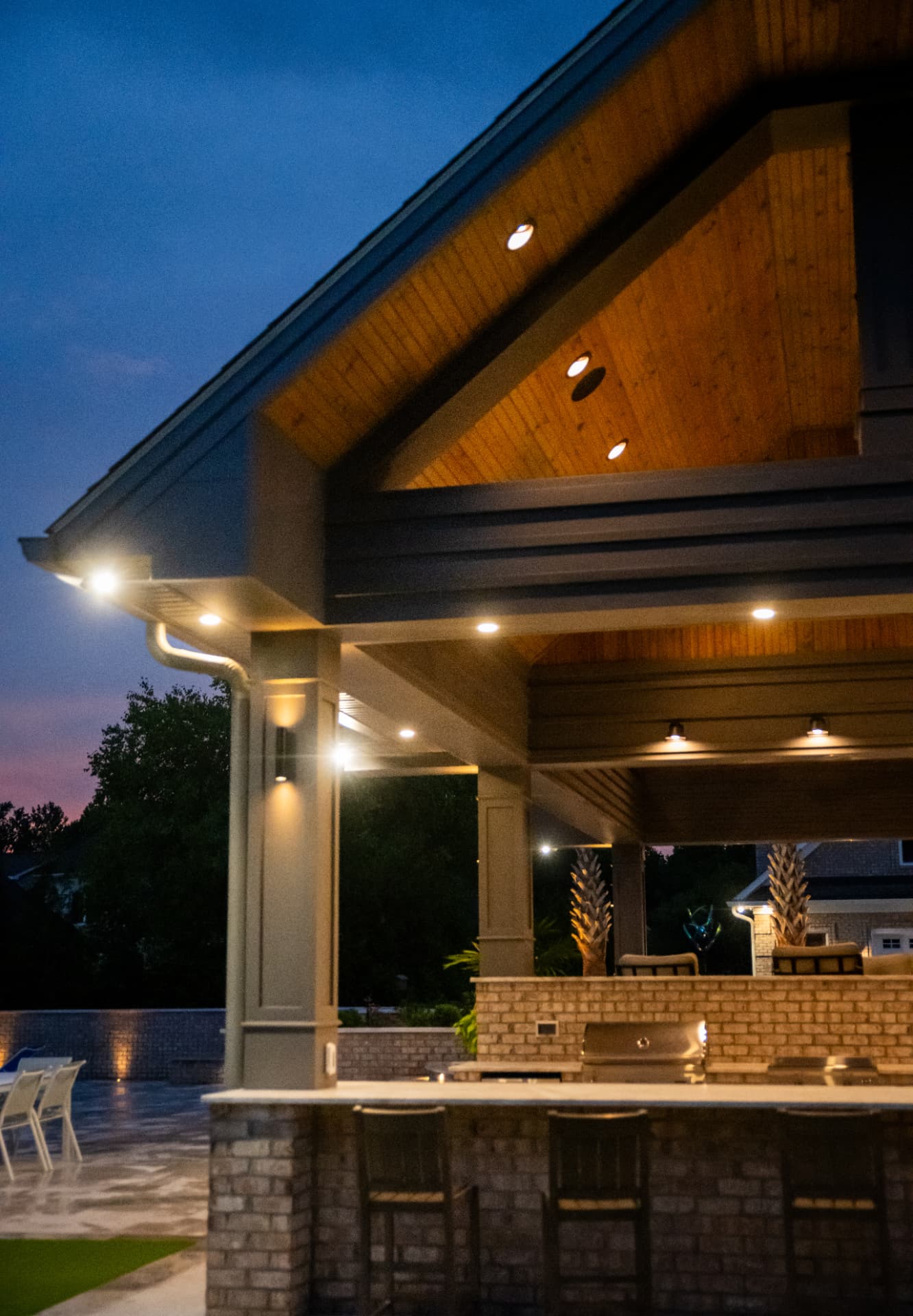 Covered pavilion bar with cedar ceiling and built-in grill lit at dusk