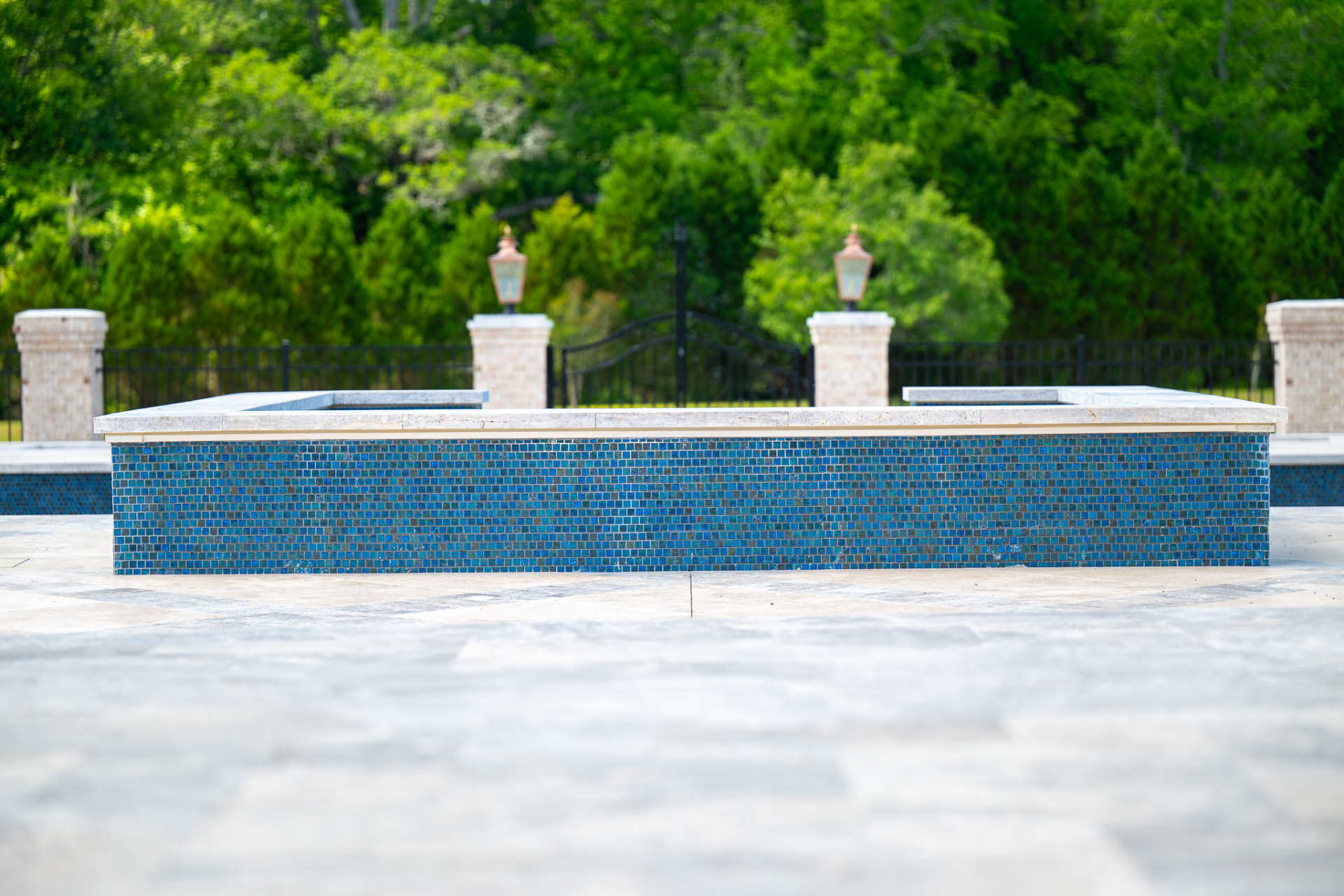 Raised spa with blue glass mosaic tile and travertine coping