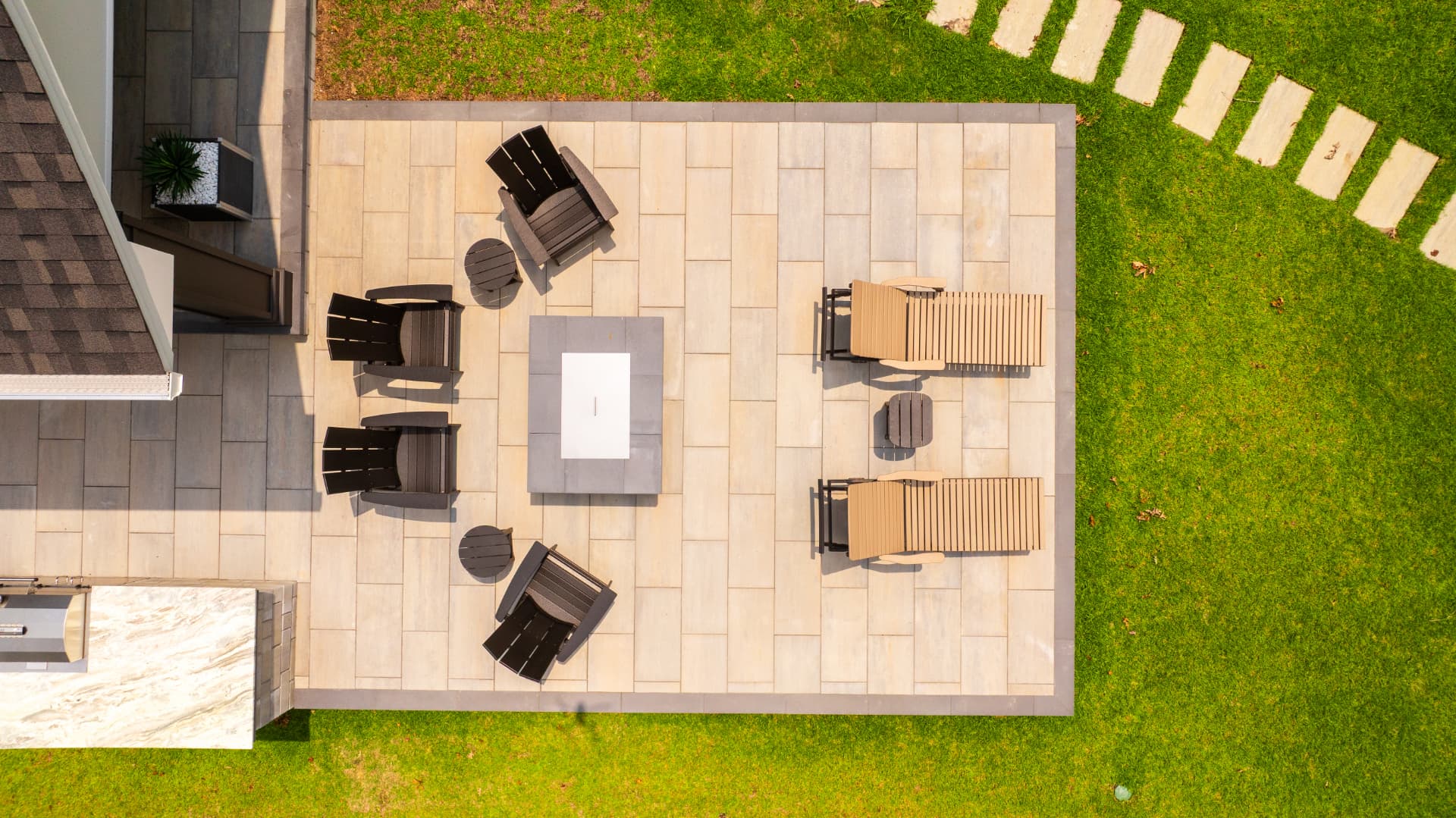 Overhead view of a rectangular paver patio with fire table, loungers, and stepping stone path