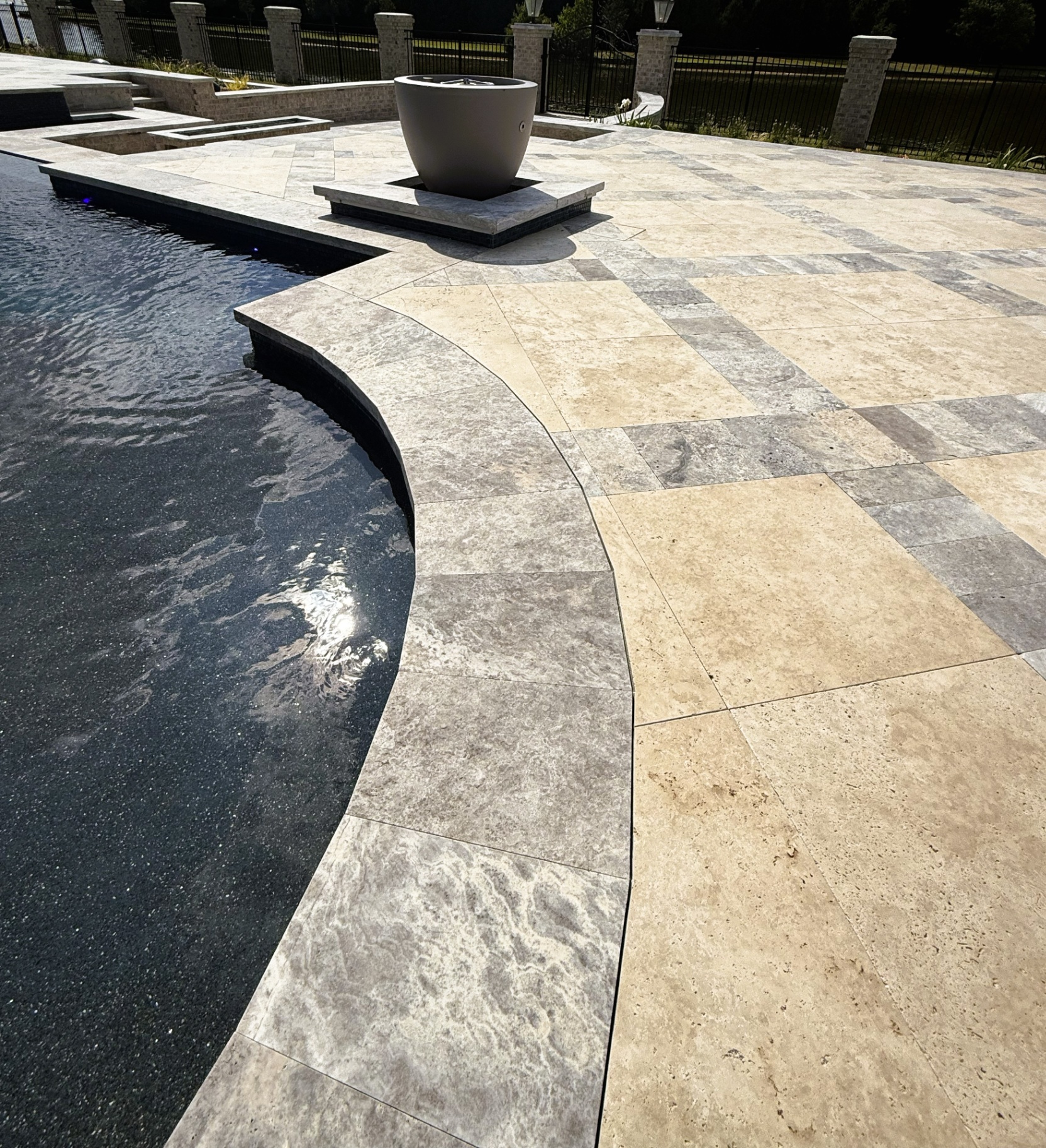 Curved travertine pool deck with tiered steps and a large central fire bowl feature
