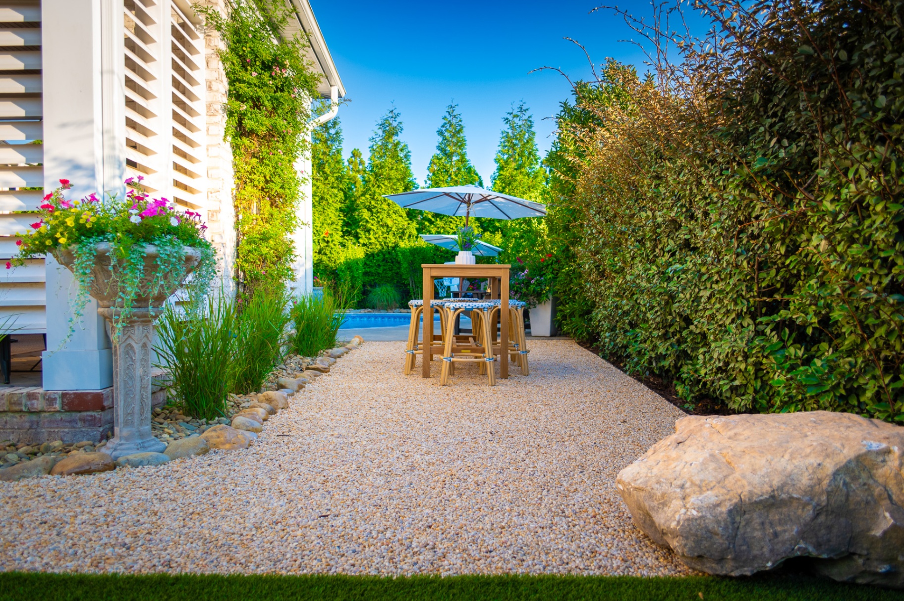 Pea gravel patio with teak bistro table between louvered wall and hedgerow