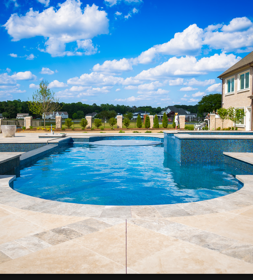 Custom Bluevue pool with blue mosaic tile and travertine decking on a bright summer day