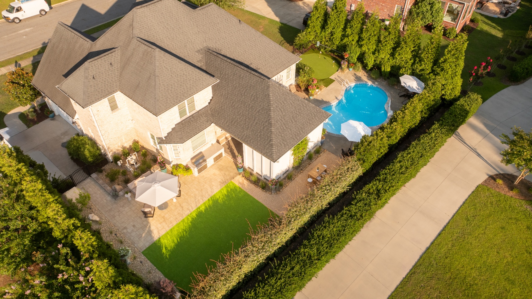Aerial view of white brick home with freeform pool, turf lawn, and paver patio